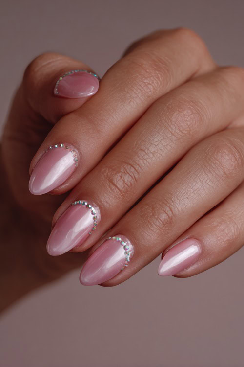 Elegant hand placing a pearl hairpin, almond nails in creamy pink with clear gloss and tiny rhinestone details along the base of each nail
