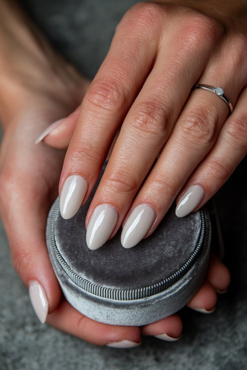 Elegant hand placing wedding ring in a velvet box, oval nails in pastel ivory with chrome tips and tiny pearls near the base of each nail 