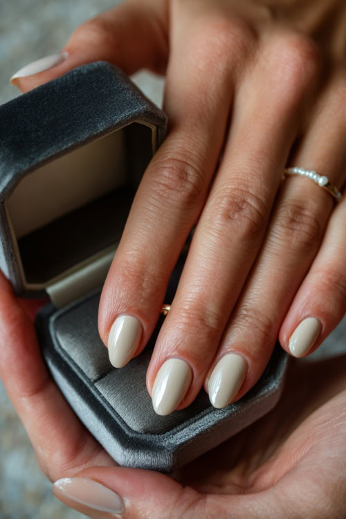 Elegant hand placing wedding ring in a velvet box, oval nails in pastel ivory with chrome tips and tiny pearls near the base of each nail