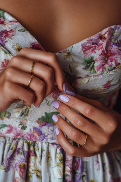 Guest’s hand adjusting a floral dress strap, short almond nails in pastel lilac with sheer glossy finish and small gold bead accents 