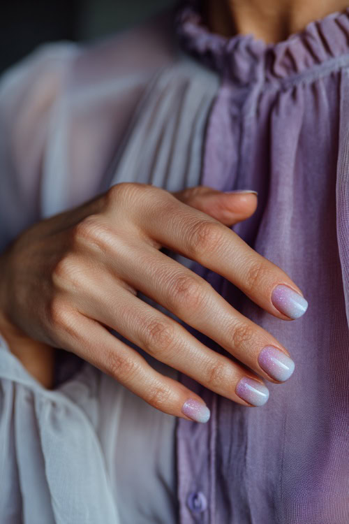 Guest’s hand gently brushing chiffon dress, short rounded nails in pastel lavender with silver glitter ombré fade on the tips