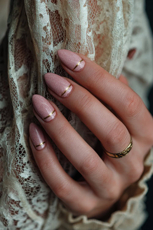 Hand brushing against vintage lace, short almond nails in pastel rose with shimmer overlay and delicate gold striping on two fingers