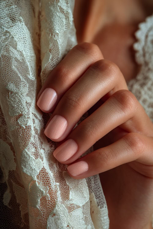 Hand gently lifting the hem of a bridal gown, ballerina nails in pale peach with marble texture and clear glossy finish