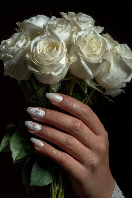 Hand holding a bouquet of white roses, ballerina-shaped nails in sheer ivory with glossy finish and delicate lace detailing on the tips