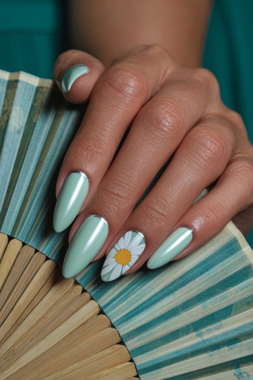 Hand holding a wedding program fan, medium almond nails in pastel mint green with chrome French tips and one accent nail featuring daisy art