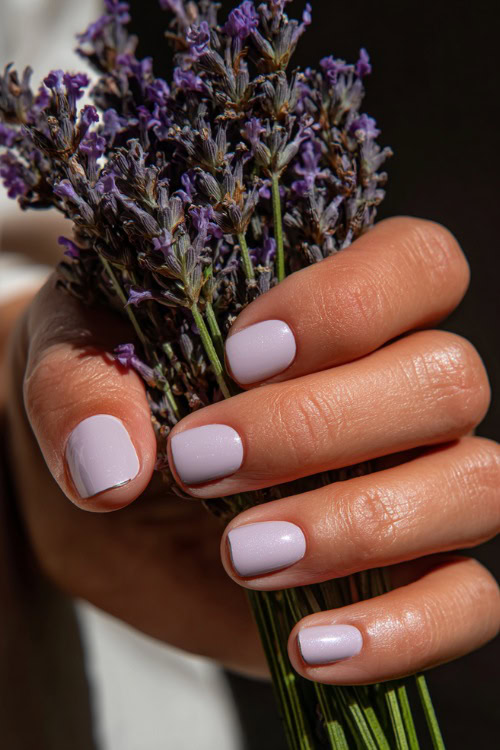 Hand holding bridal bouquet stem, square-shaped nails in pastel lavender with shimmer overlay and minimal silver line art near the base