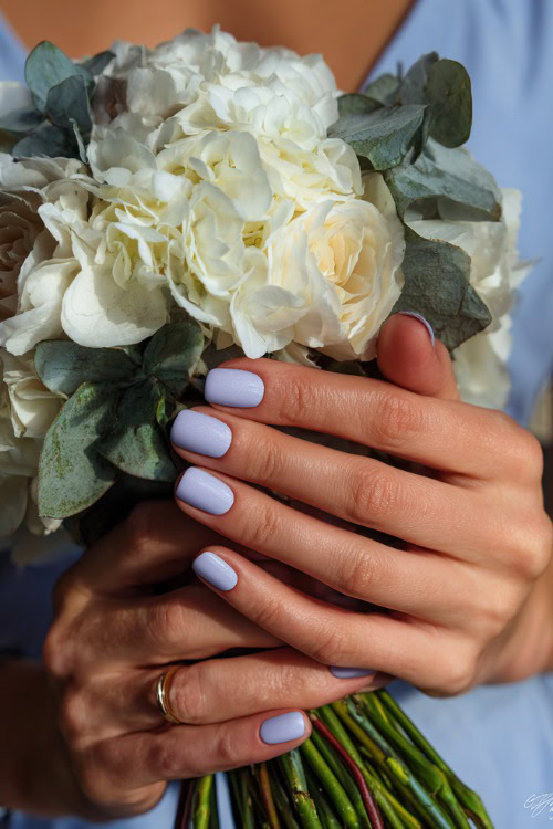 Hand holding bridal bouquet stem, square-shaped nails in pastel lavender with shimmer overlay and minimal silver line art near the base