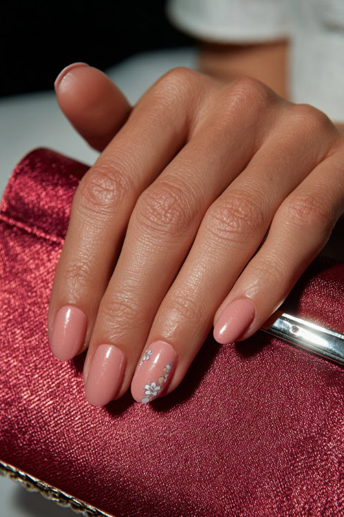 Hand resting beside silk clutch, short almond nails in sheer pink with chrome shimmer and tiny silver floral decals on two finger
