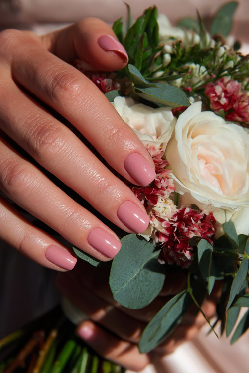 Hand tying ribbon on bouquet, short square nails in pastel pink with a satin topcoat and delicate floral stamping on two fingers 