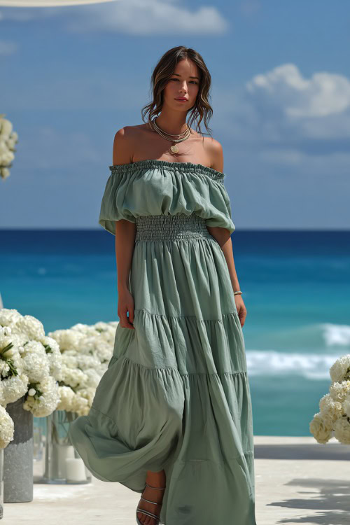 Elegant woman wearing a flowy off-the-shoulder maxi dress with tiered layers, soft green color, metallic sandals, standing near a seaside wedding with white flowers and ocean waves