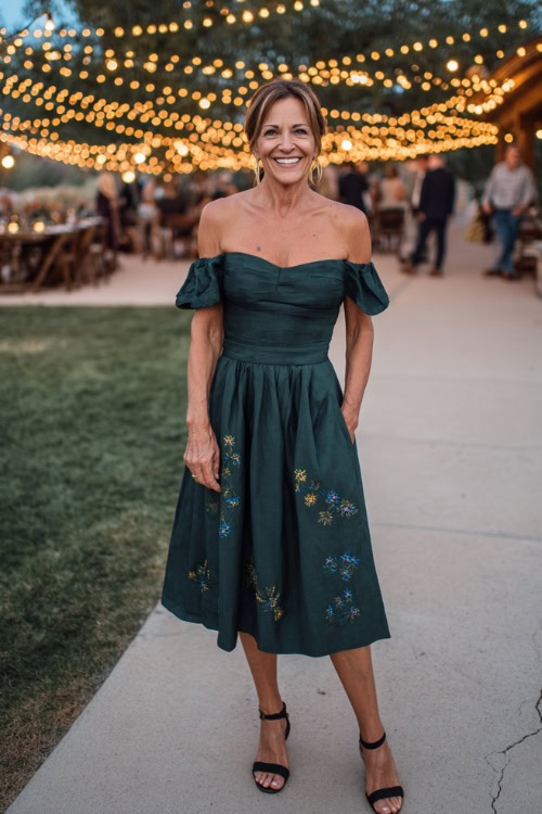Fashionable woman over 50 wearing an off-the-shoulder midi-length wedding guest dress in dark green, subtle floral embroidery, and slingback heels 