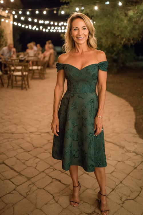 Fashionable woman over 50 wearing an off-the-shoulder midi-length wedding guest dress in dark green, subtle floral embroidery, and slingback heels 