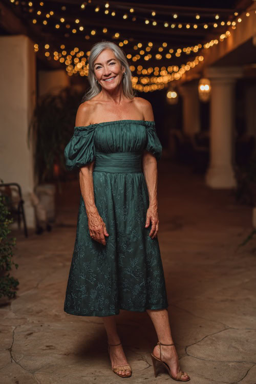 Fashionable woman over 50 wearing an off-the-shoulder midi-length wedding guest dress in dark green, subtle floral embroidery, and slingback heels