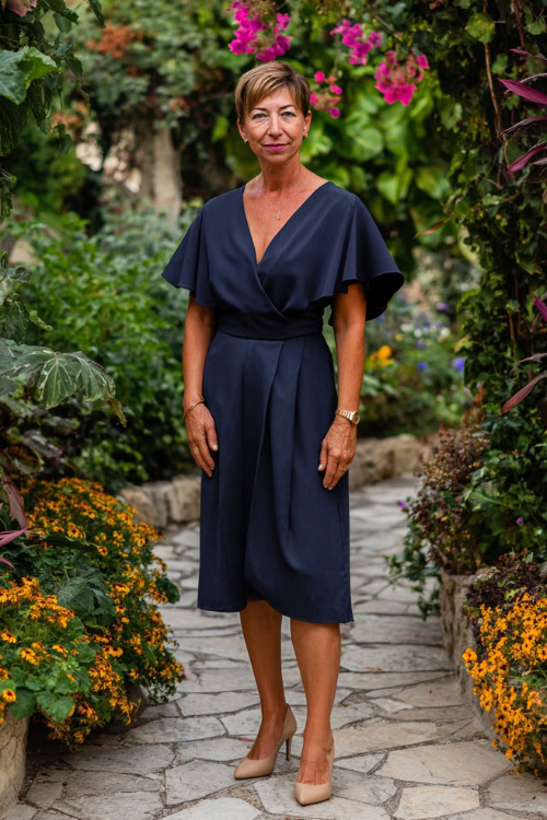 Full body of a confident woman over 50 wearing an elegant navy blue midi-length wedding guest dress with flutter sleeves, a defined waistline 