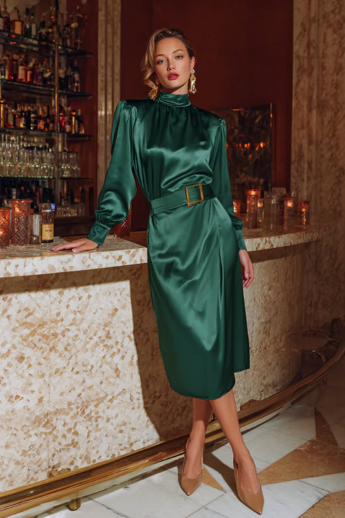 Stylish woman in a high-neck emerald green satin midi dress with long sleeves and a belted waist, paired with gold earrings and pointed toe heels 