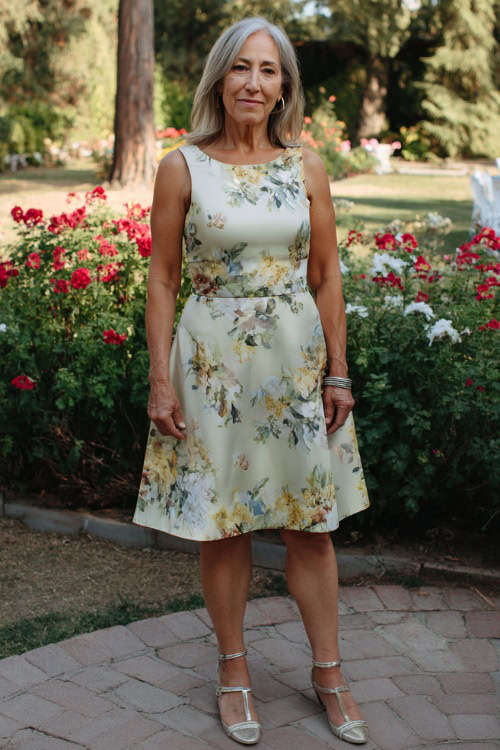 Stylish woman over 50 in a sleeveless A-line wedding guest dress with soft floral prints, knee-length hem, and silver strappy sandals 