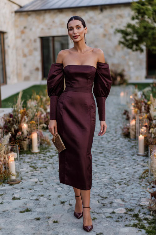 Woman in a deep wine-colored midi wedding guest dress with structured puff sleeves and a square neckline, styled with classic heels and a clutch